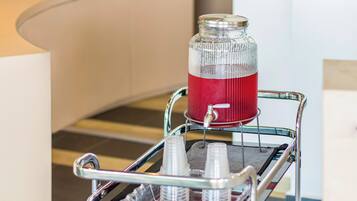 A beverage cart with a glass jar filled with a red drink, a water dispenser, and several plastic cups.