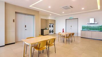 A modern dining area with wooden tables and chairs, a kitchen with appliances, and a fire extinguisher.