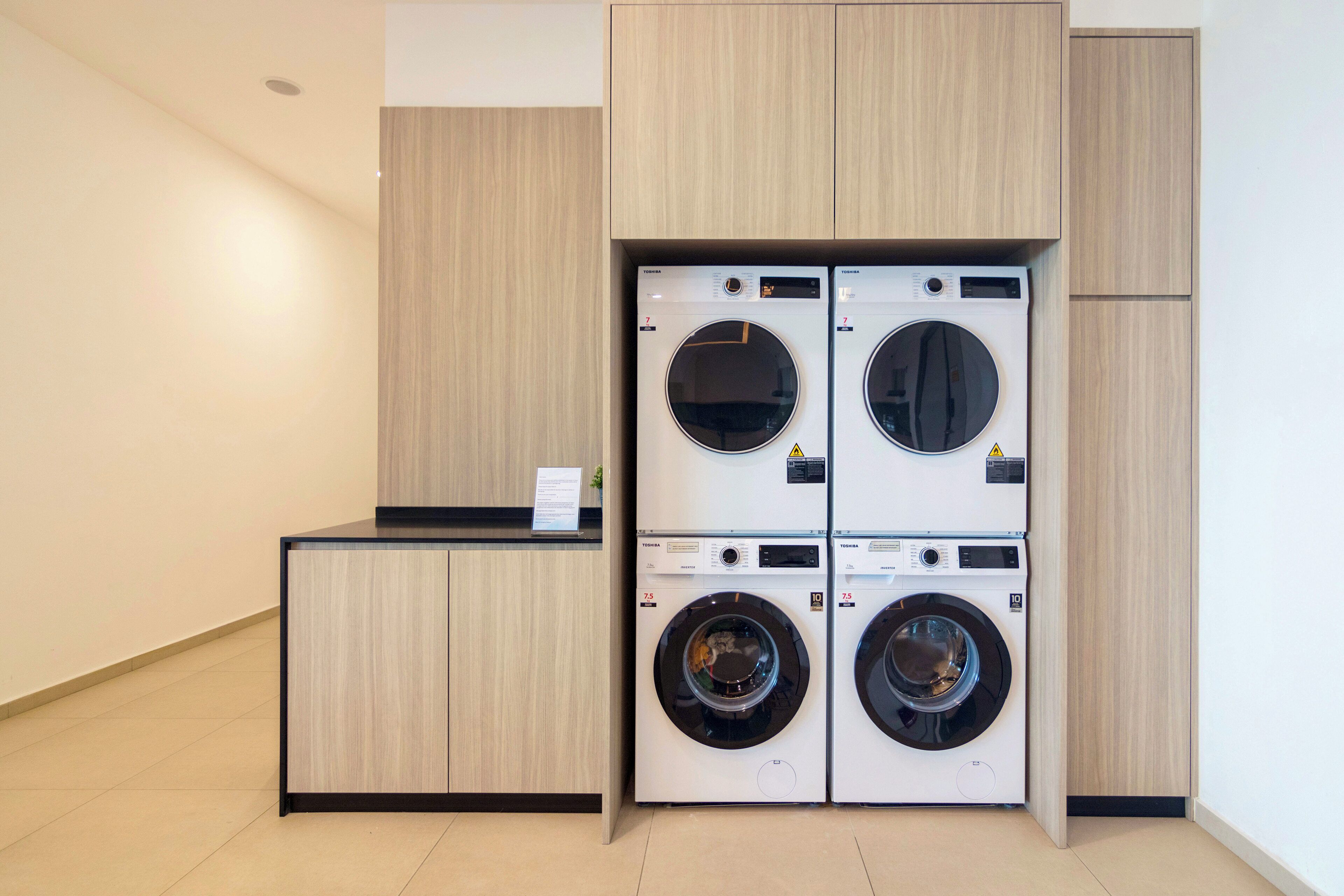 A laundry room with four stacked front-loading washing machines and a counter with a sign.