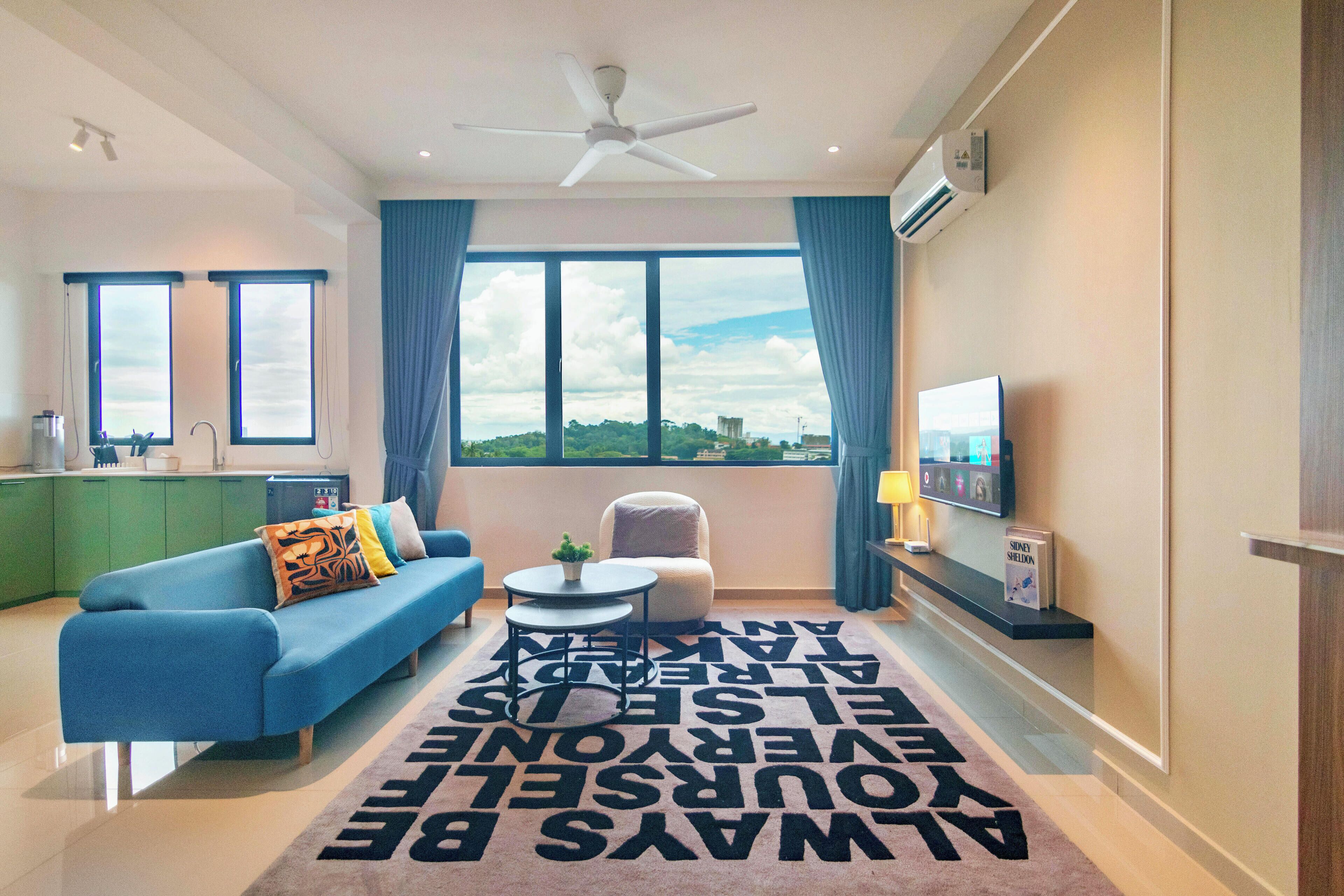 A modern living room with a blue sofa, a small round table, a ceiling fan, and a large window with curtains.