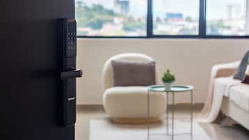 A modern room with a black door, a white chair, a small round table with a plant, and a view of a cityscape through large windows.