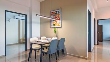 A modern dining area with a table set for four, a hanging light fixture, and a colorful abstract artwork on the wall.