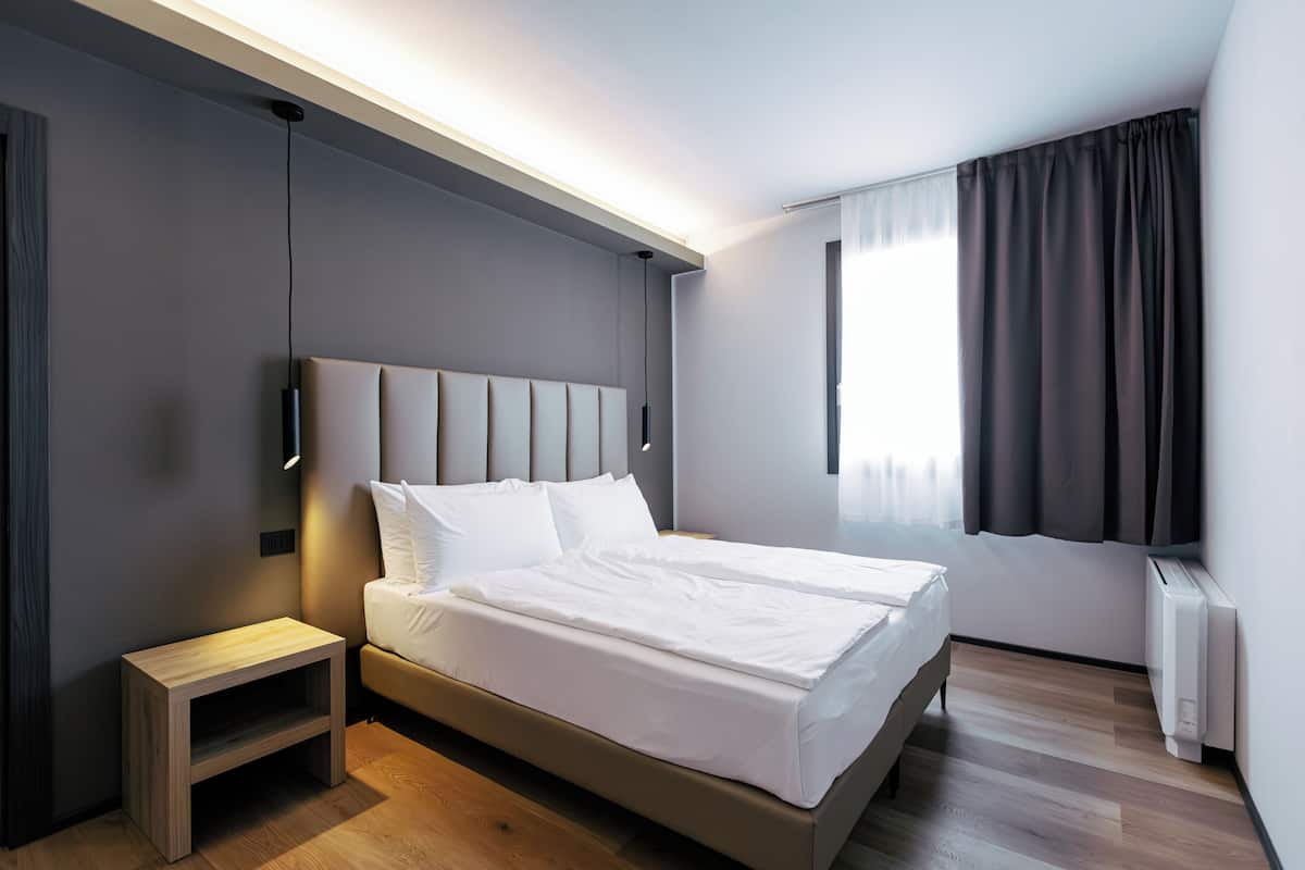 A modern hotel room with a large bed, bedside table, and a window with curtains.