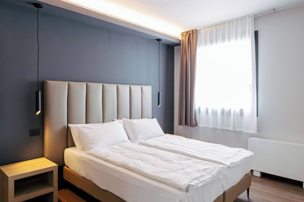Une chambre moderne avec un grand lit, des tables de chevet, une commode et une fenêtre avec des rideaux.