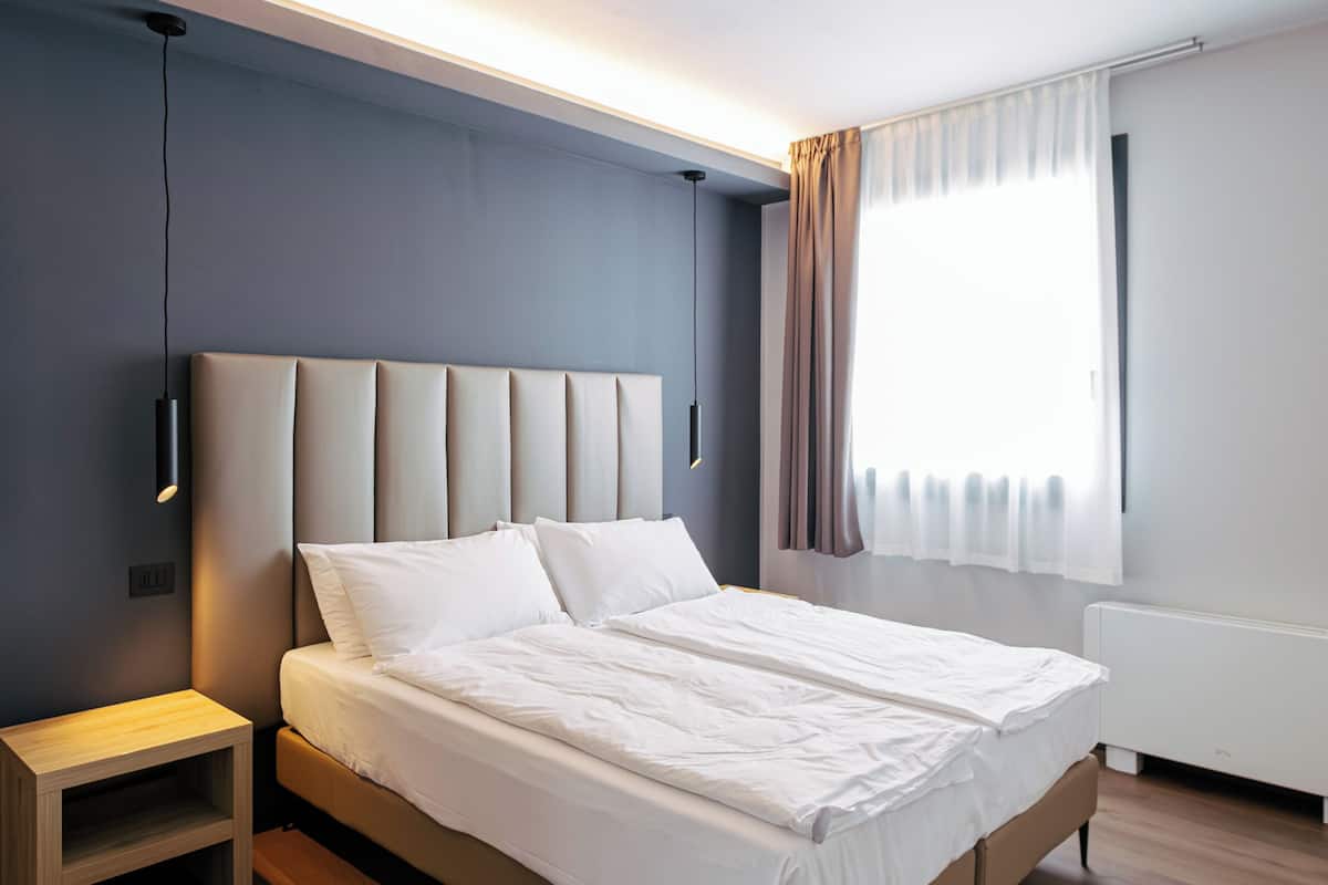 A modern bedroom with a large bed, bedside tables, a nightstand, and a window with curtains.