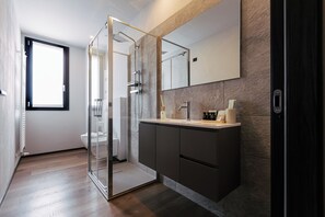 Ein modernes Badezimmer mit Duschkabine aus Glas, einem großen Spiegel und einem dunklen Waschtisch.