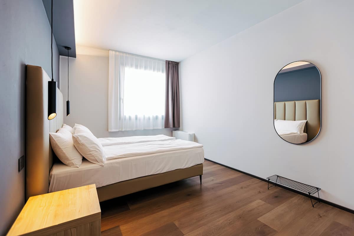 A modern bedroom with a bed, bedside table, and a wall-mounted mirror.
