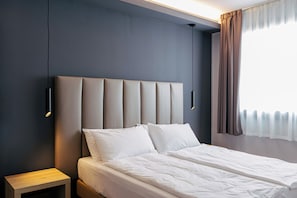 A modern hotel room with a large bed, a bedside table, and a wall-mounted light fixture.
