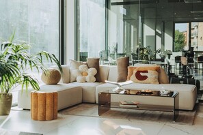 A modern living room with a sectional sofa, a glass coffee table, and a large window offering a view of the city. - Ah Virgilio Apartments Resort (Mantua)