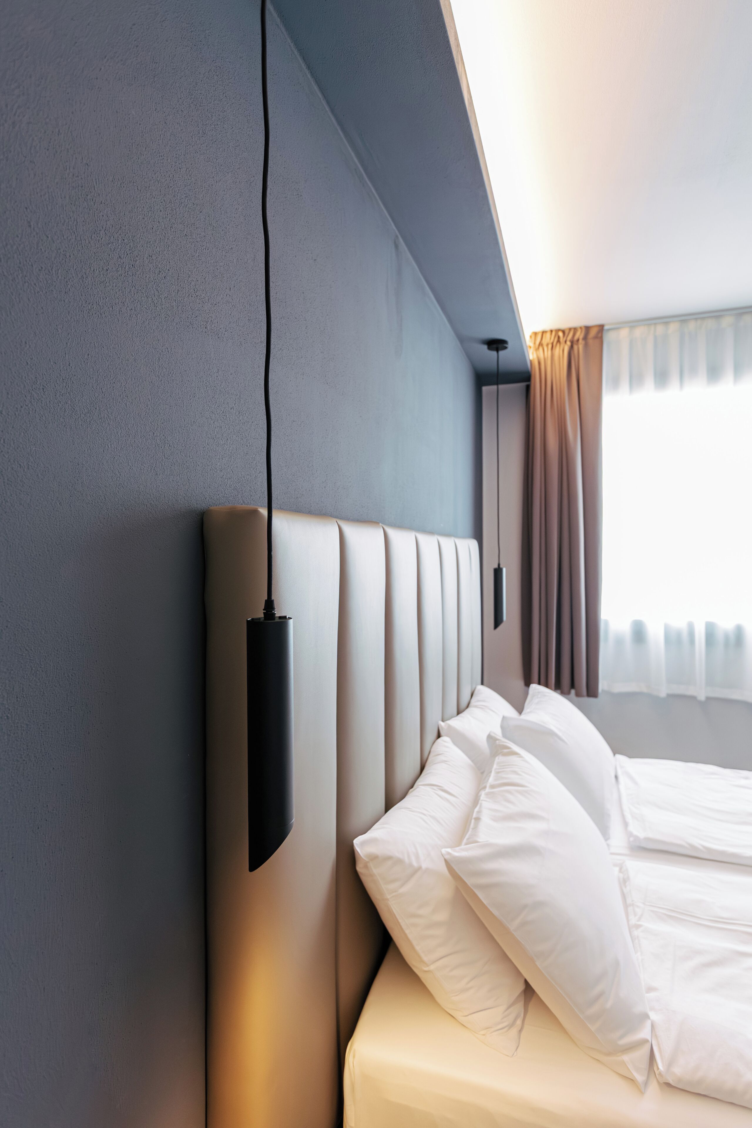 Une chambre d’hôtel moderne dotée d’un grand lit, d’une tête de lit avec éclairage intégré et offrant une vue sur la ville par la fenêtre.