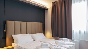 A modern hotel room with a bed, bedside table, and a view of the outdoors.