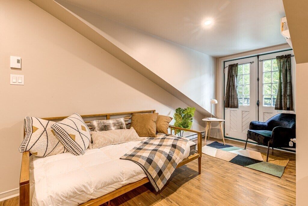 Ein Schlafzimmer mit einem Bett, einem kleinen Tisch, einem Sessel und einem Fenster mit Vorhängen.