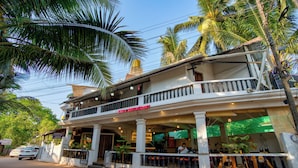 A two-story bar and restaurant with a balcony, surrounded by palm trees. - Swizel Nook Stay (Calangute)