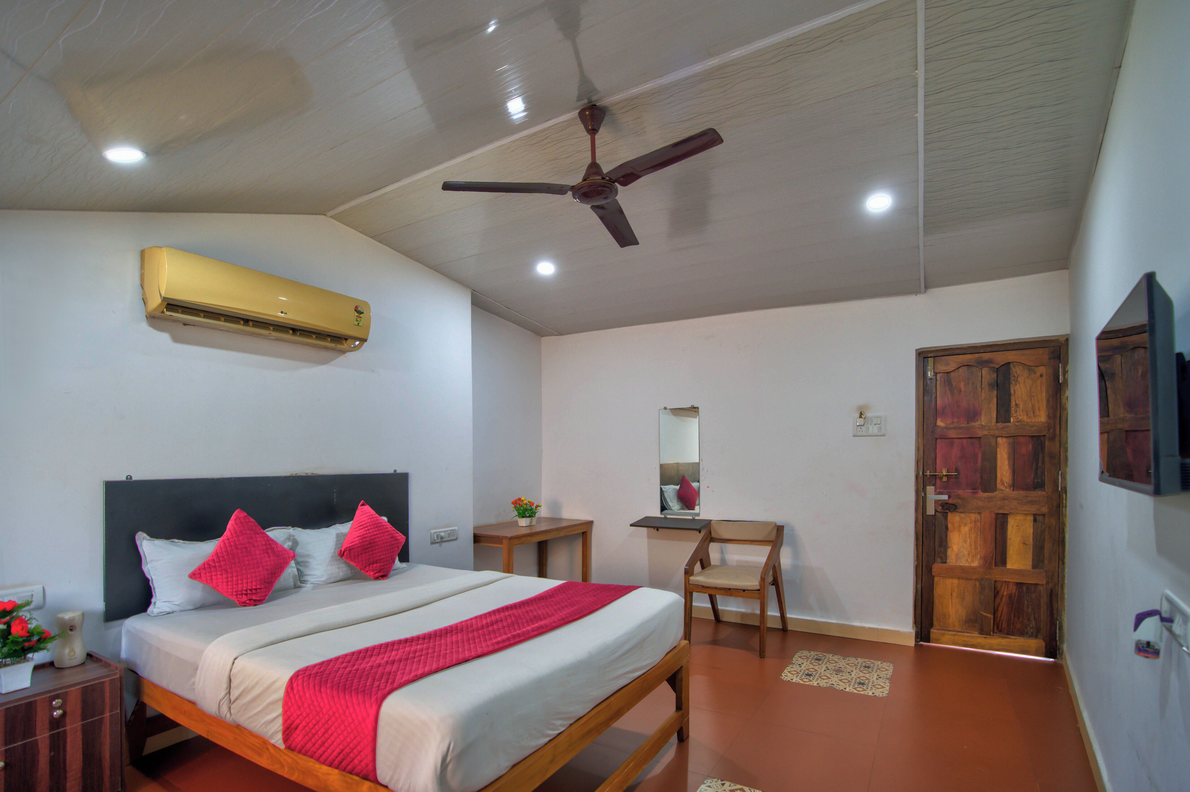 A bedroom with a bed, a desk, a chair, an air conditioner, and a wooden door.