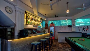 A bar area with a pool table, bar stools, a refrigerator, and a clock on the wall. - Swizel Nook Stay (Calangute)