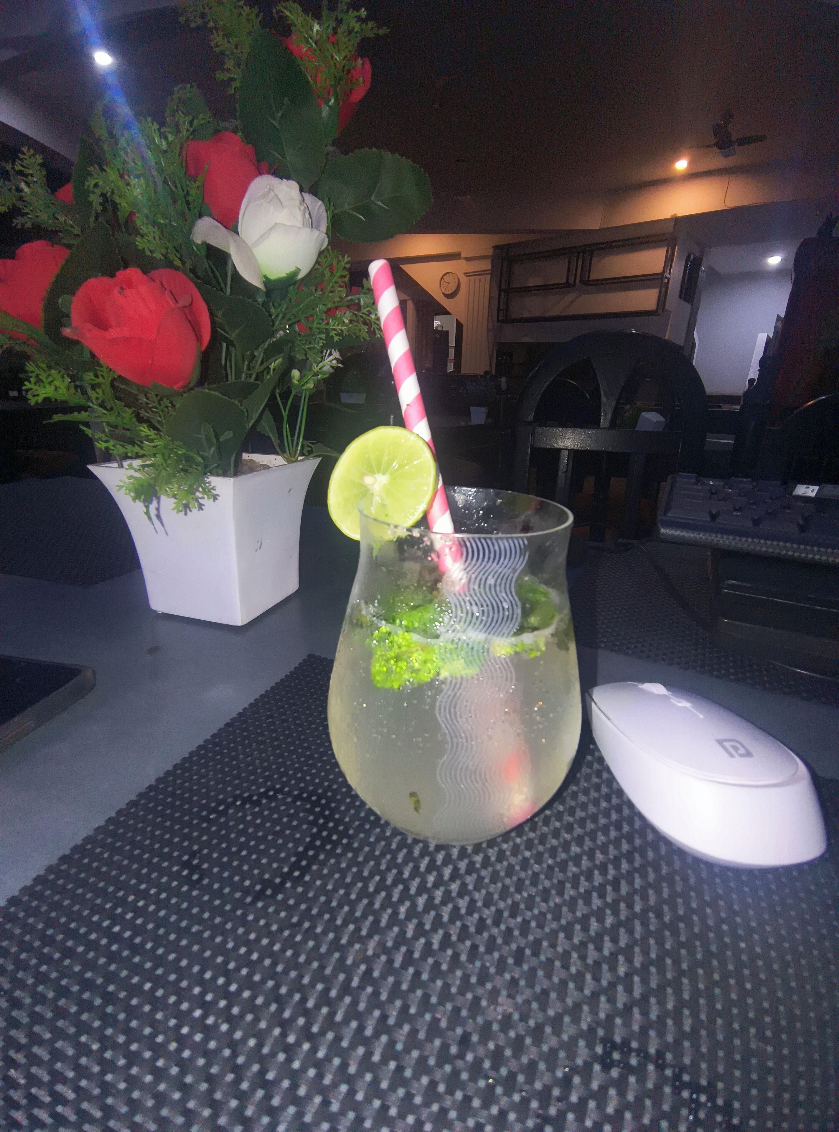 Un verre contenant une tranche de citron vert et une paille rayée, posé sur une table, à côté d’une souris d’ordinateur blanche.