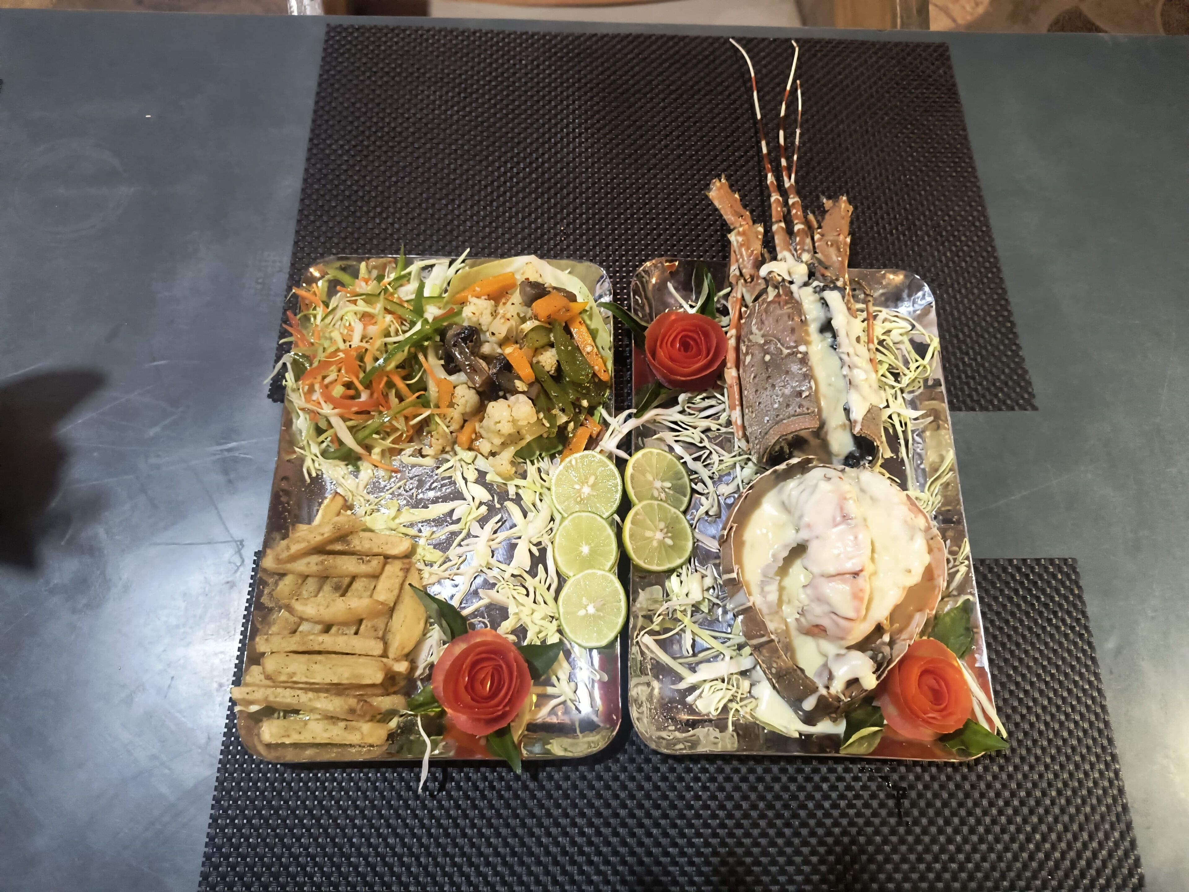 A tray of food including vegetables, a lobster, and a rose.