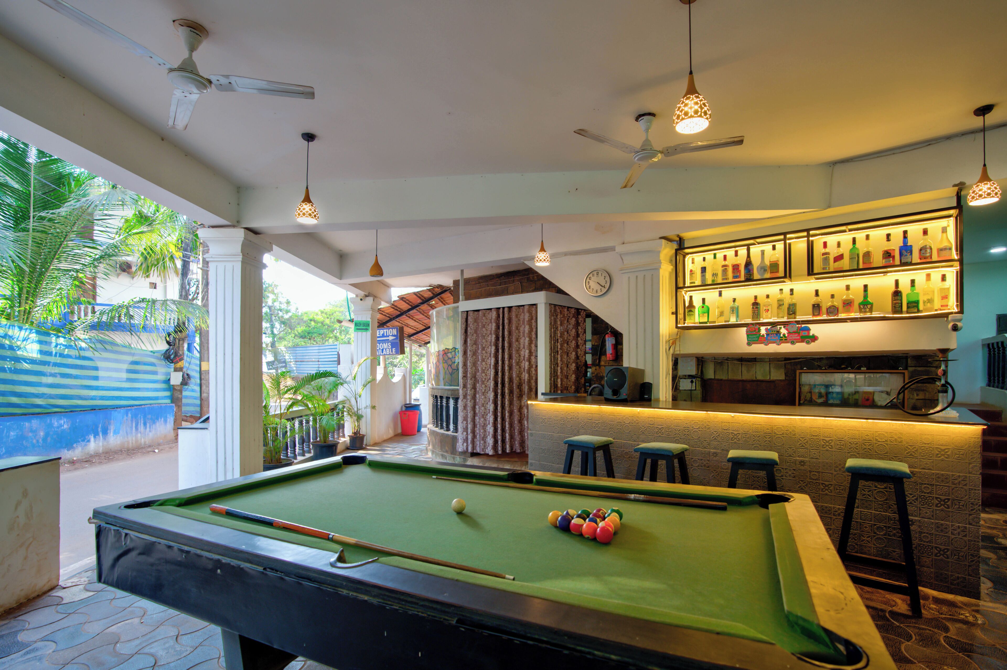 A pool table with a cue stick, a bar area with bottles, and a ceiling fan.
