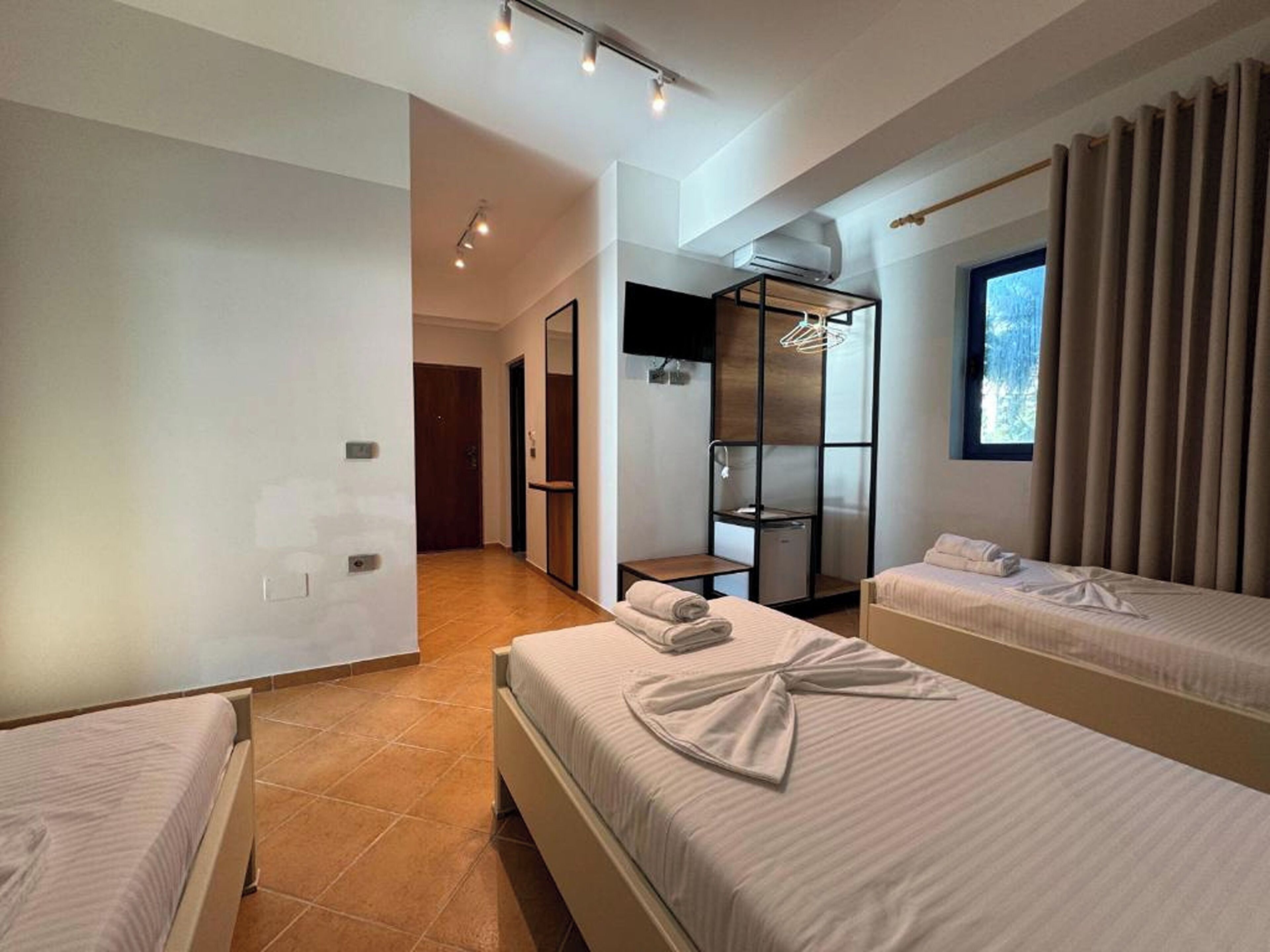 Ein Hotelzimmer mit zwei Betten, einem Kleiderschrank, einem Fernseher und einem Fenster mit Vorhängen.