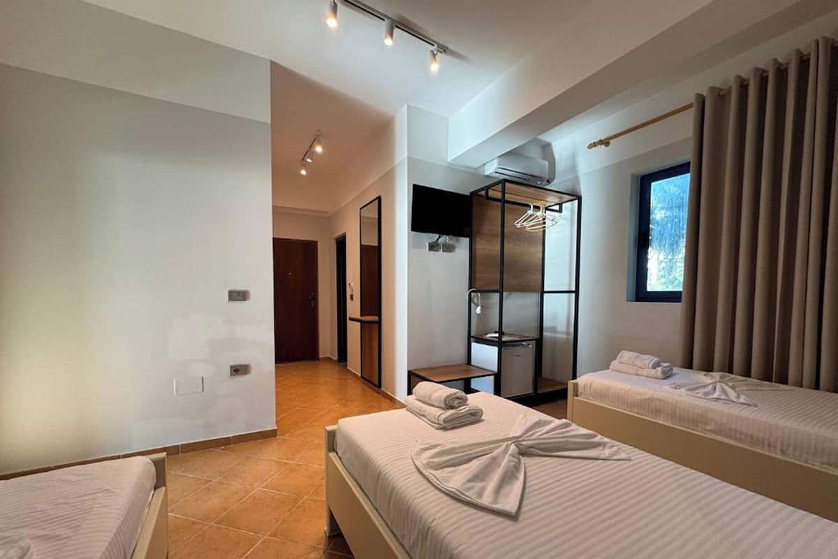 A hotel room with two beds, a wardrobe, a TV, and a window with curtains.