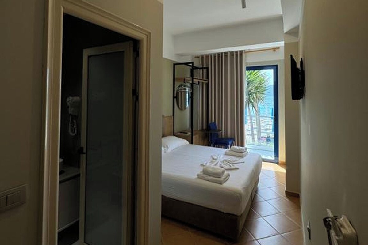 A hotel room with a bed, a shower, a balcony with a view, and a television mounted on the wall.