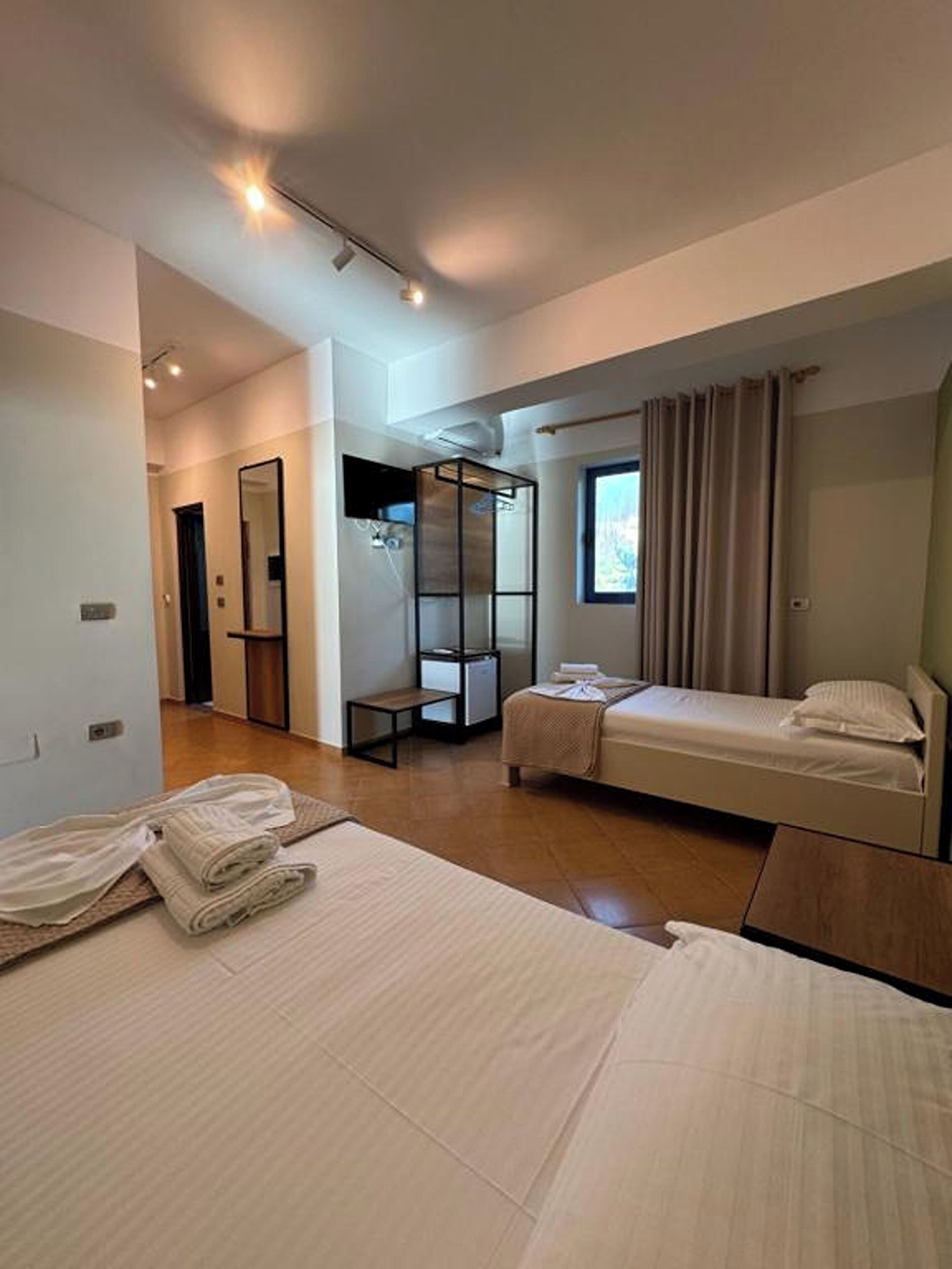 Ein modernes Hotelzimmer mit zwei Betten, einem begehbaren Kleiderschrank, einem großen Spiegel und einem Fenster mit Vorhängen.
