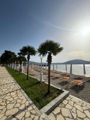 A beachside walkway with stone tiles, palm trees, and sun loungers. - Hotel Cekodhima (Orikum)