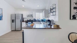 A modern kitchen with white cabinets, a stainless steel refrigerator, and a granite countertop. - Chic & Modern Home with Pool Table, BBQ, and MORE (North Las Vegas)
