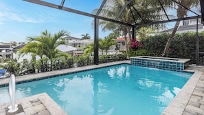 A swimming pool with a tiled edge, surrounded by a stone deck and palm trees.