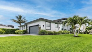 A modern two-story house with a grey garage door, surrounded by well-maintained grass and palm trees. - Spectacular home with western exposure, heated pool and spa (Marco Island)