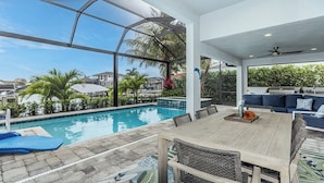 Une piscine sur le toit avec vue sur les palmiers et les maisons, une table en bois avec des chaises et un canapé bleu.