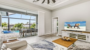 A spacious living room with a large TV, a pool view, and a balcony.
