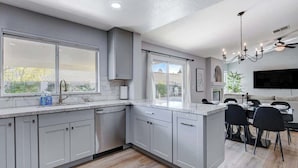 A modern kitchen with grey cabinets, a large island, and a dining area with black chairs. - 6BR Paradise w/ Pool, Pool table | Lux Retreat (North Las Vegas)