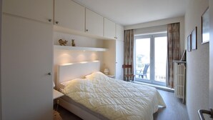 A bedroom with a bed, built-in shelving, a chair, and a view of the outdoors through a sliding door. - Sleek Apartment w/ Dual Terraces (De Haan)