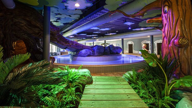 Un'area giochi per bambini con piscina, alberi artificiali e un soffitto decorato con nuvole.