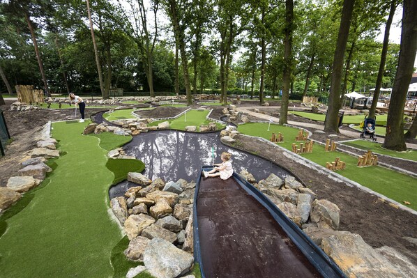 Un campo da mini golf con manto erboso verde, un ostacolo d'acqua e un bambino che gioca.