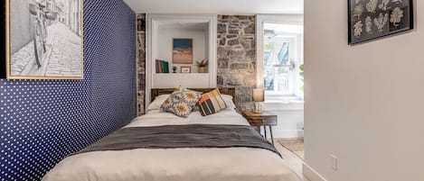 Un dormitorio con cama, mesita de noche, lámpara e impresión botánica enmarcada en la pared.