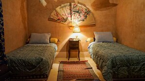 Ein kleiner, gemütlicher Raum mit zwei Betten, einem traditionellen Ventilator und einer Nachttischlampe.