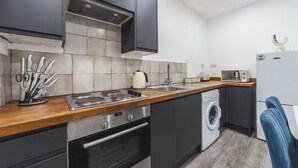 Une cuisine compacte équipée d’une cuisinière, d’un évier et d’un lave-linge, avec des meubles de couleur sombre et un plan de travail en bois.