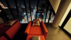 Une chambre d’hôtel moderne avec vue sur la ville, comprenant deux canapés rouges et une grande fenêtre.