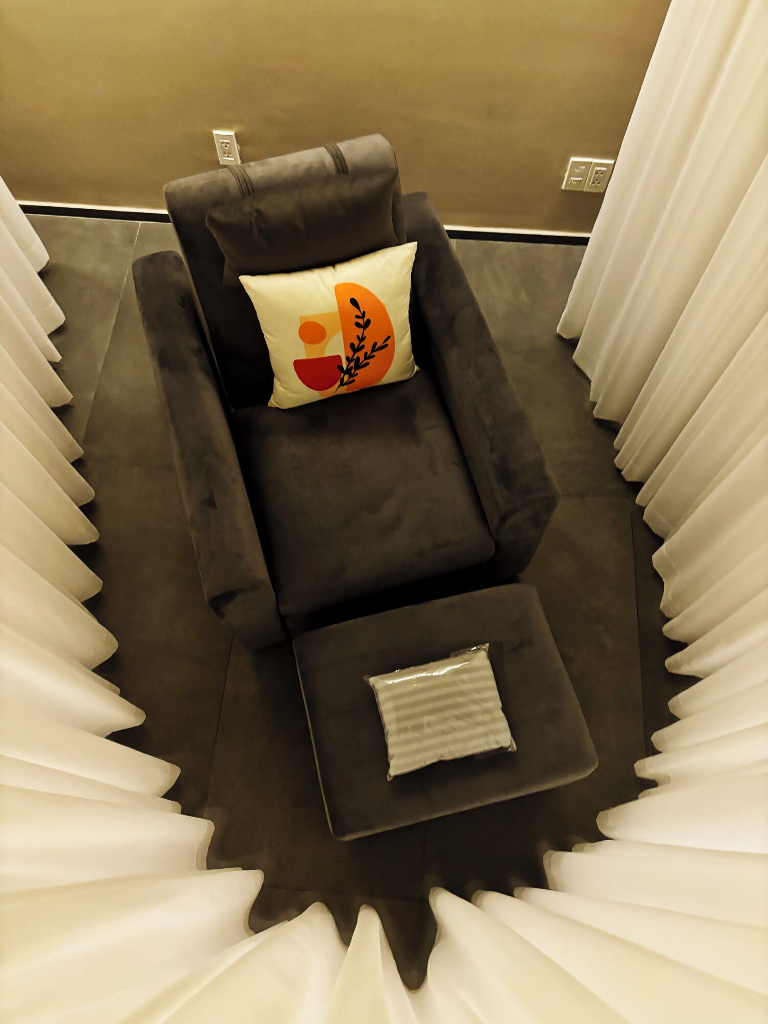 A massage chair with a pillow and a small ottoman in a room with white curtains.