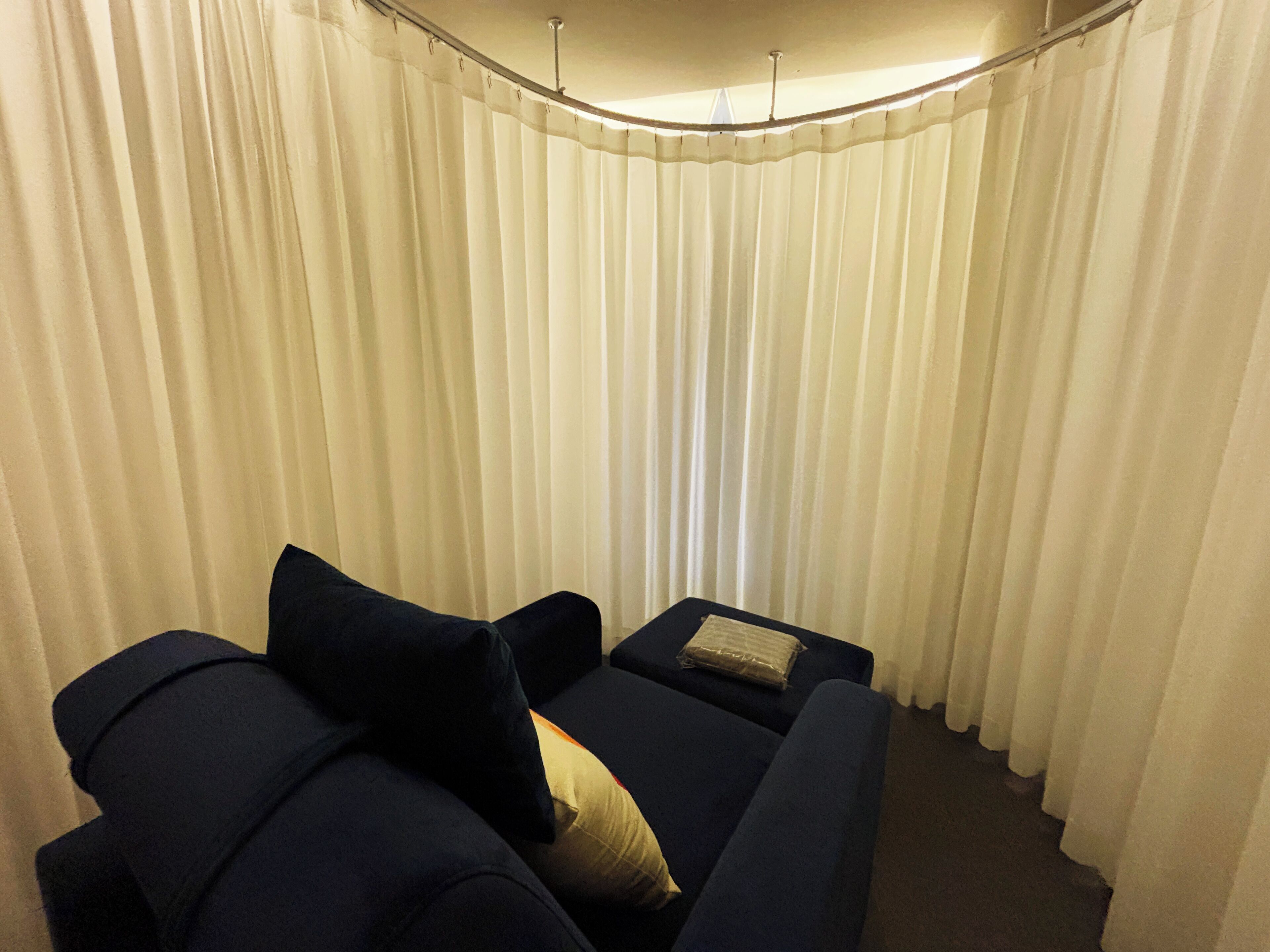 A living room with a dark blue sofa, a small table, and a white curtain backdrop.