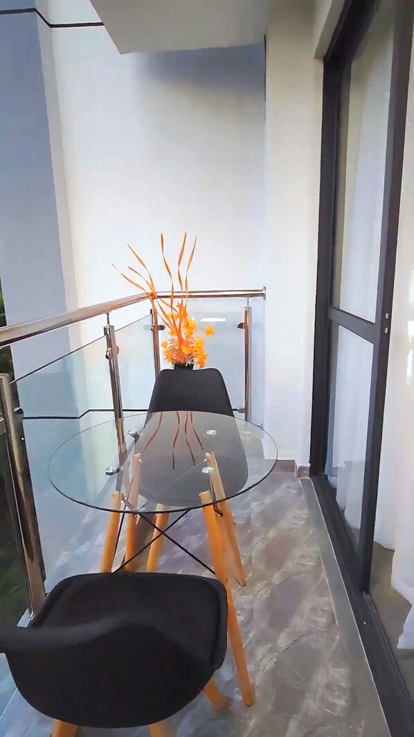 Un espace repas moderne avec une table en verre, des chaises noires et un vase décoratif orné de fleurs oranges.