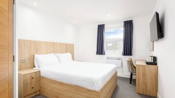 Habitación de hotel con cama de madera, escritorio con silla, televisor montado en la pared y ventana con cortinas.