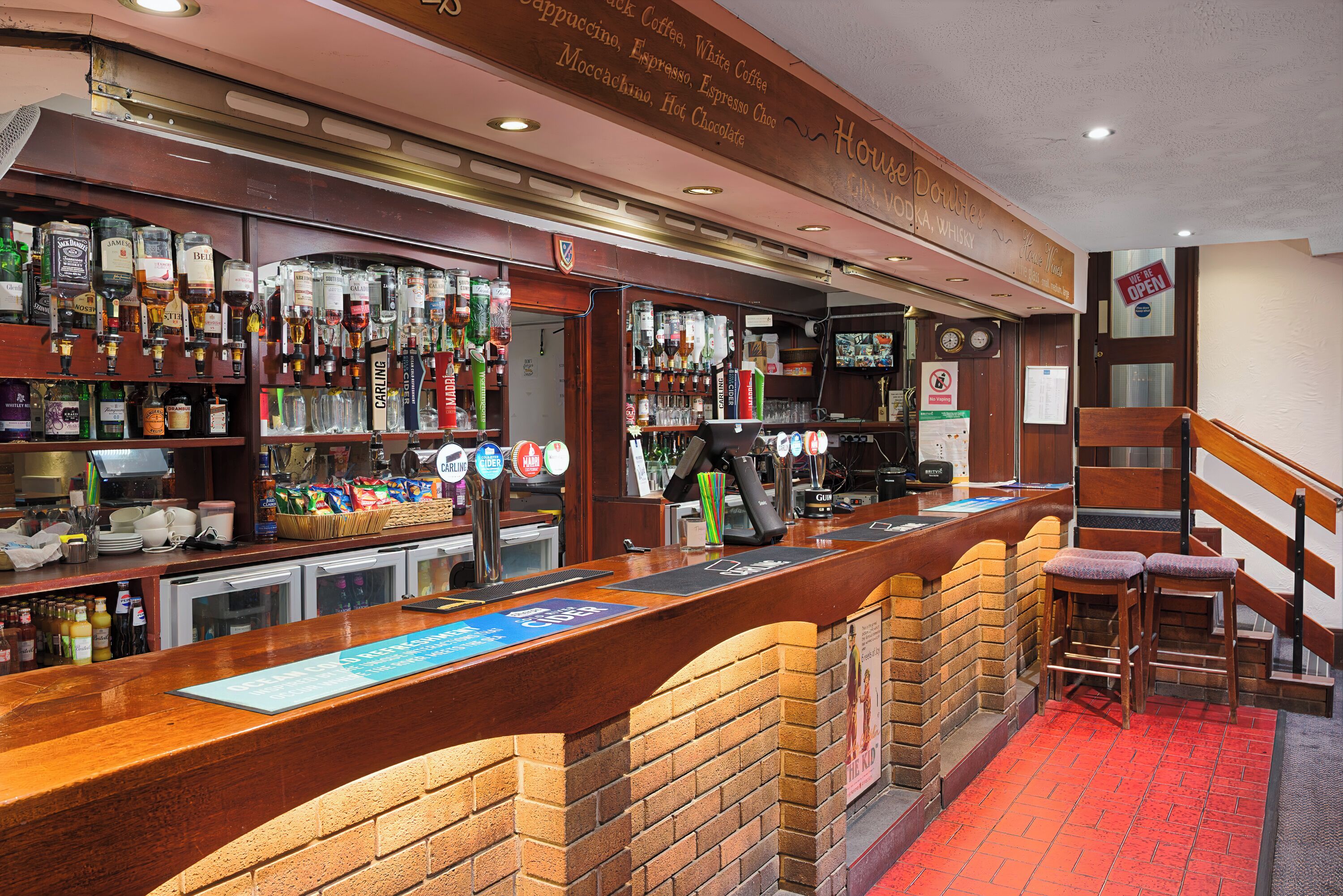 A bar with a brick counter, shelves of liquor bottles, and stools.