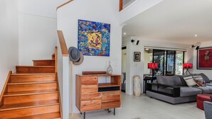 A spacious living area with a wooden staircase, a grey sofa, and a large painting on the wall. - Your Ultimate Beachside Escape in the Heart of Casuarina! (Casuarina)