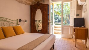Un dormitorio con cama, espejo, armario, televisor sobre un mueble y puerta que da a un espacio exterior.