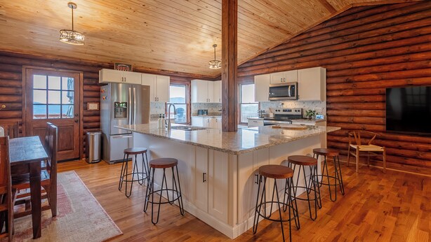 A spacious kitchen with wooden walls, a large island with stools, stainless steel appliances, and a view through the window. - Scenic 4BR retreat with valley views, minutes from Blacksburg and Lane Stadium, sleeps 12 (Blacksburg)