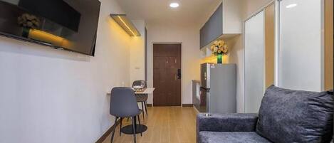 Espaço compacto com sofá, mesa de jantar com cadeiras, TV de tela plana na parede e geladeira.