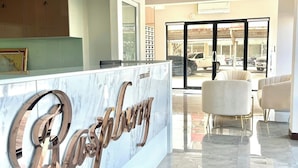 A modern reception area with a marble reception desk, a glass door leading to a parking area, and a seating area with two chairs. - Raspberry Mansion (Bang Sao Thong)